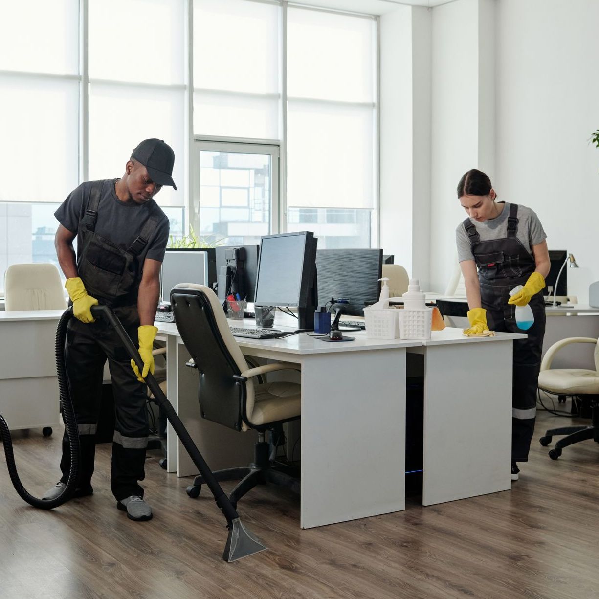 a man and a woman are cleaning an office with a vacuum cleaner .