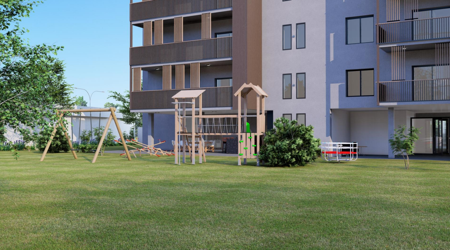 Parque infantil frente a un edificio de varios pisos con balcones. Césped y árboles en primer plano.