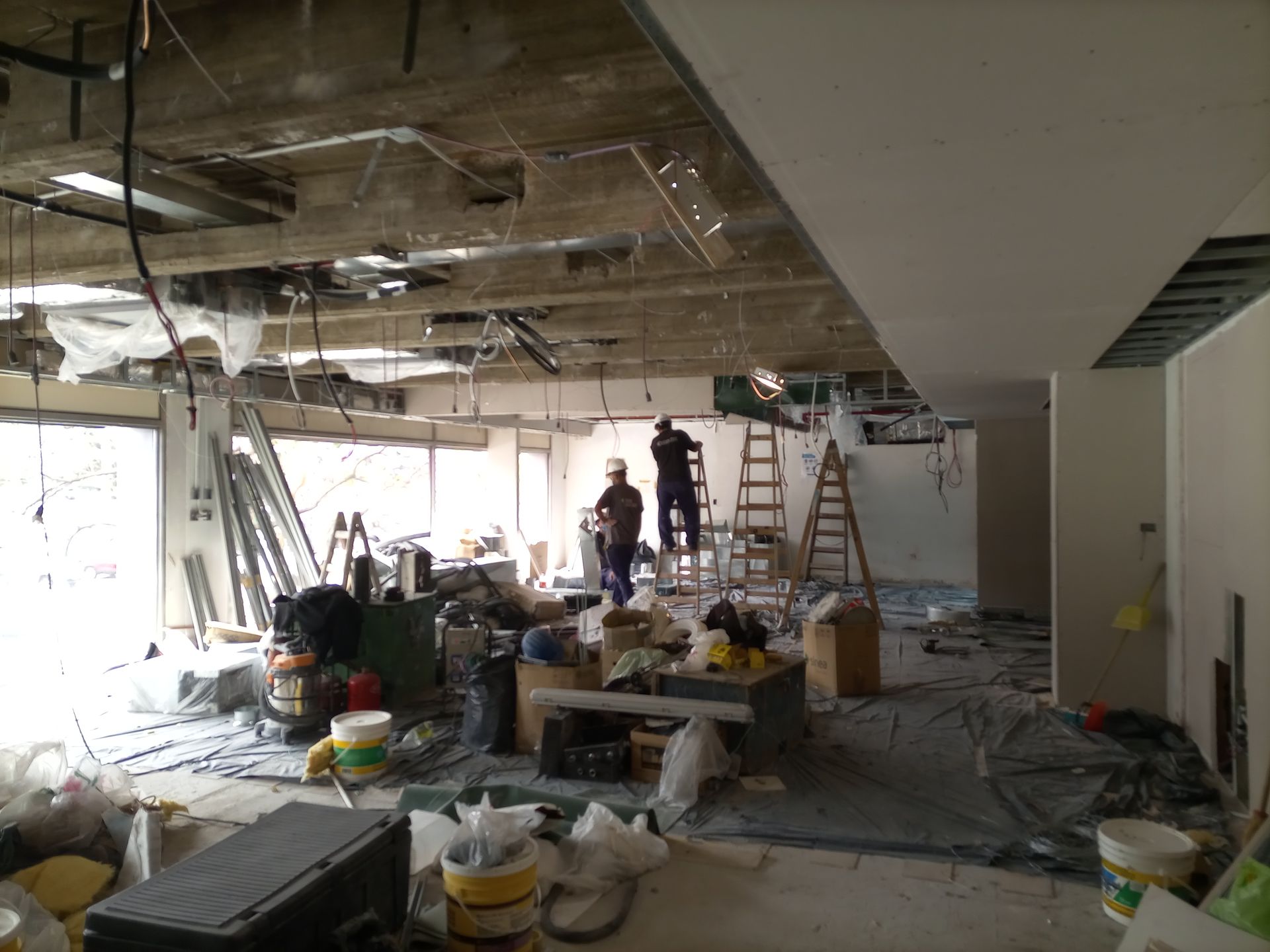 Sitio de construcción: Trabajadores dentro de una habitación con techo expuesto, herramientas, escombros y ventana brillante.