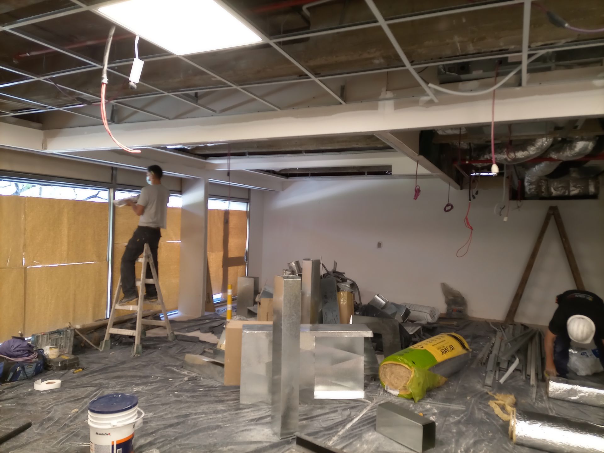 Obra: obreros instalando techo y conductos. Un hombre en una escalera, otro en el suelo.