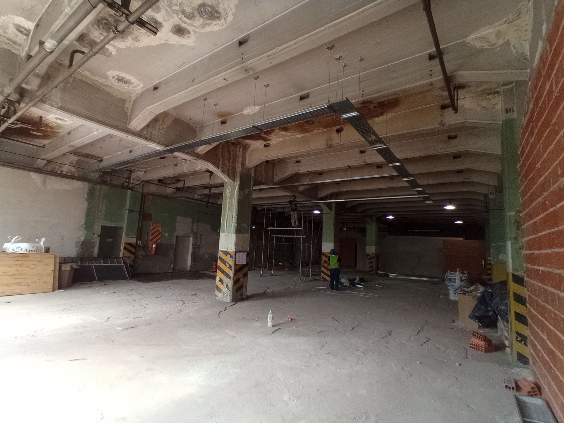 Interior de un gran espacio industrial sin terminar con pilares de hormigón, escombros de construcción y tuberías expuestas.