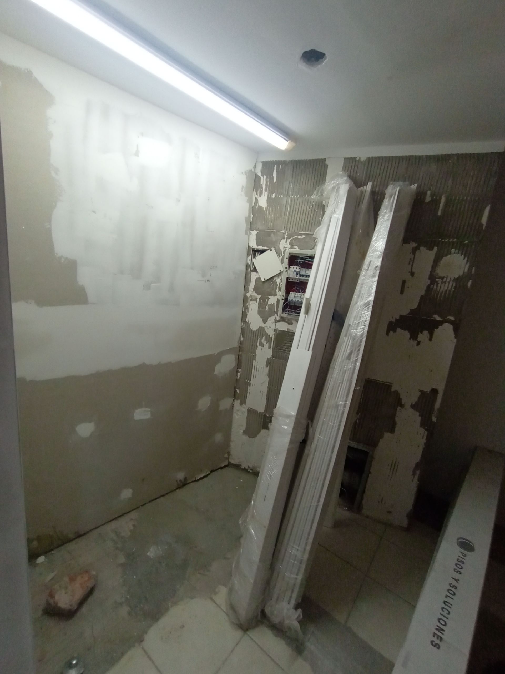 Interior de una habitación en construcción; las paredes están parcialmente terminadas, con molduras apoyadas contra ellas.