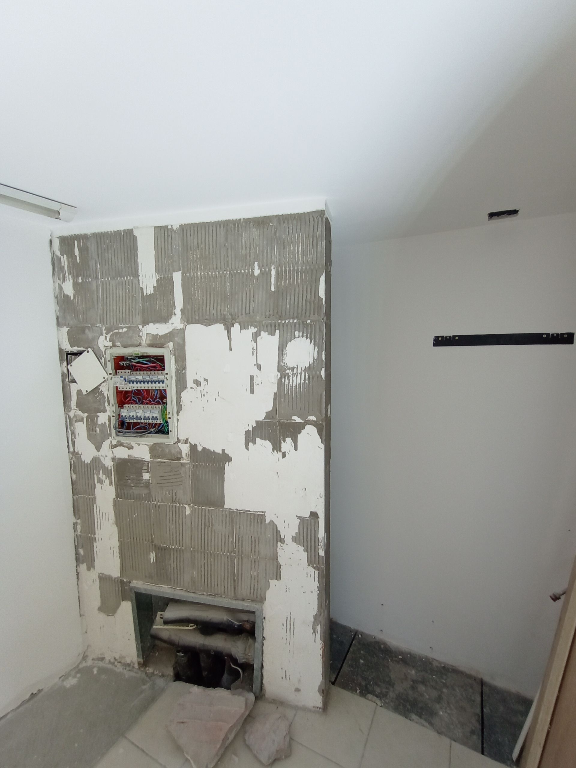 Habitación en construcción, chimenea y paredes sin terminar. Mortero gris visible, cuadro eléctrico, pintura blanca