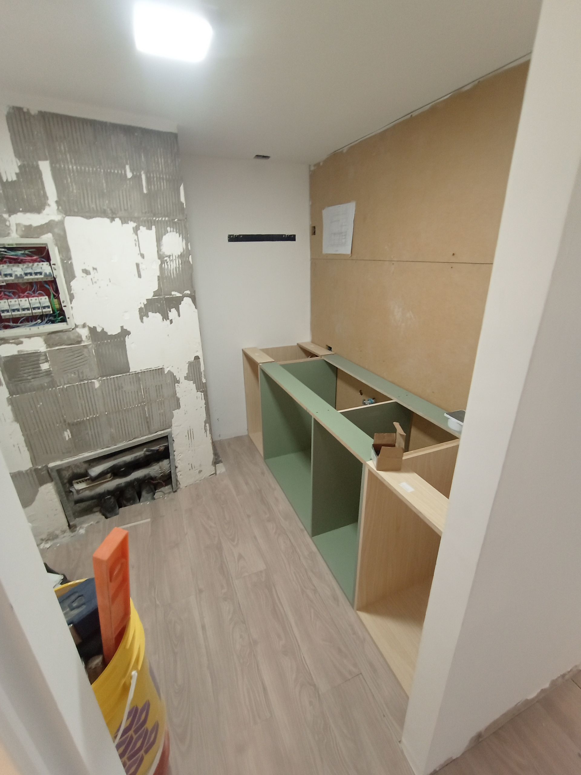 Renovación del baño en proceso. Armarios de madera y paredes sin terminar, con tuberías expuestas y azulejos dañados.