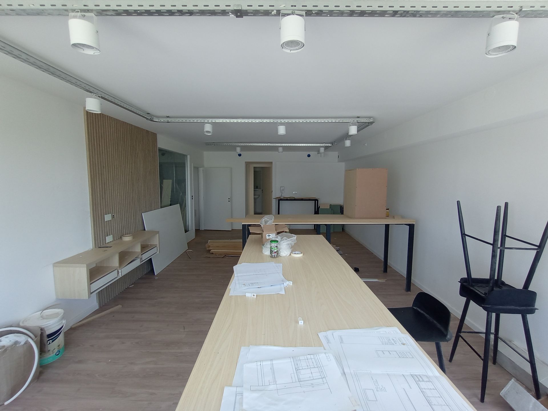 Una oficina vacía con materiales de construcción y muebles, iluminación brillante, combinación de colores madera y blanco.