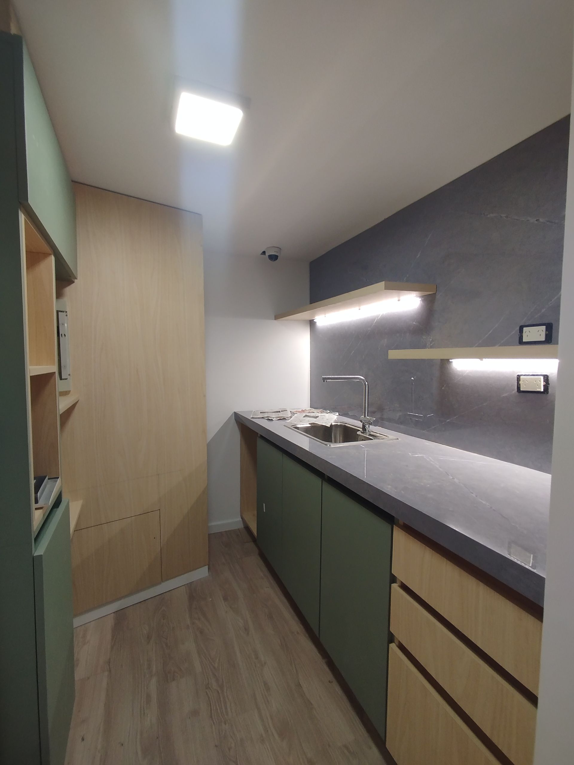 Cocina moderna con gabinetes verdes, paneles de madera y encimera oscura.