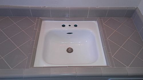 a white sink is sitting on top of a tiled counter .