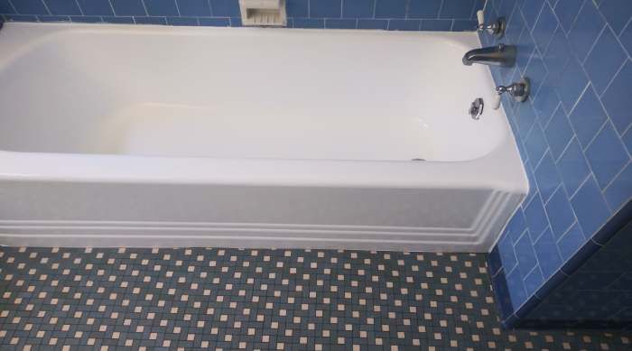 a bathtub in a bathroom with blue tiles on the wall and floor .