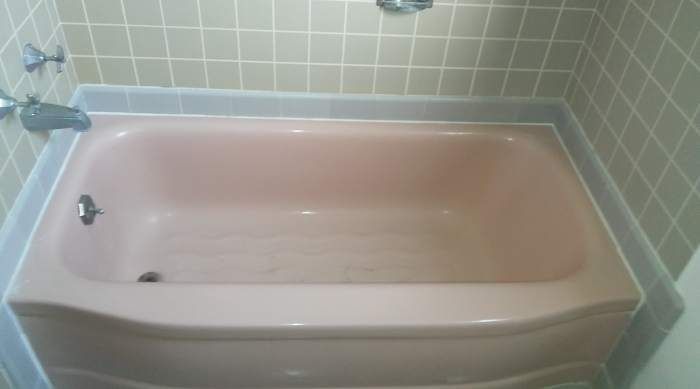 a pink bathtub is sitting in a bathroom next to a tiled wall .