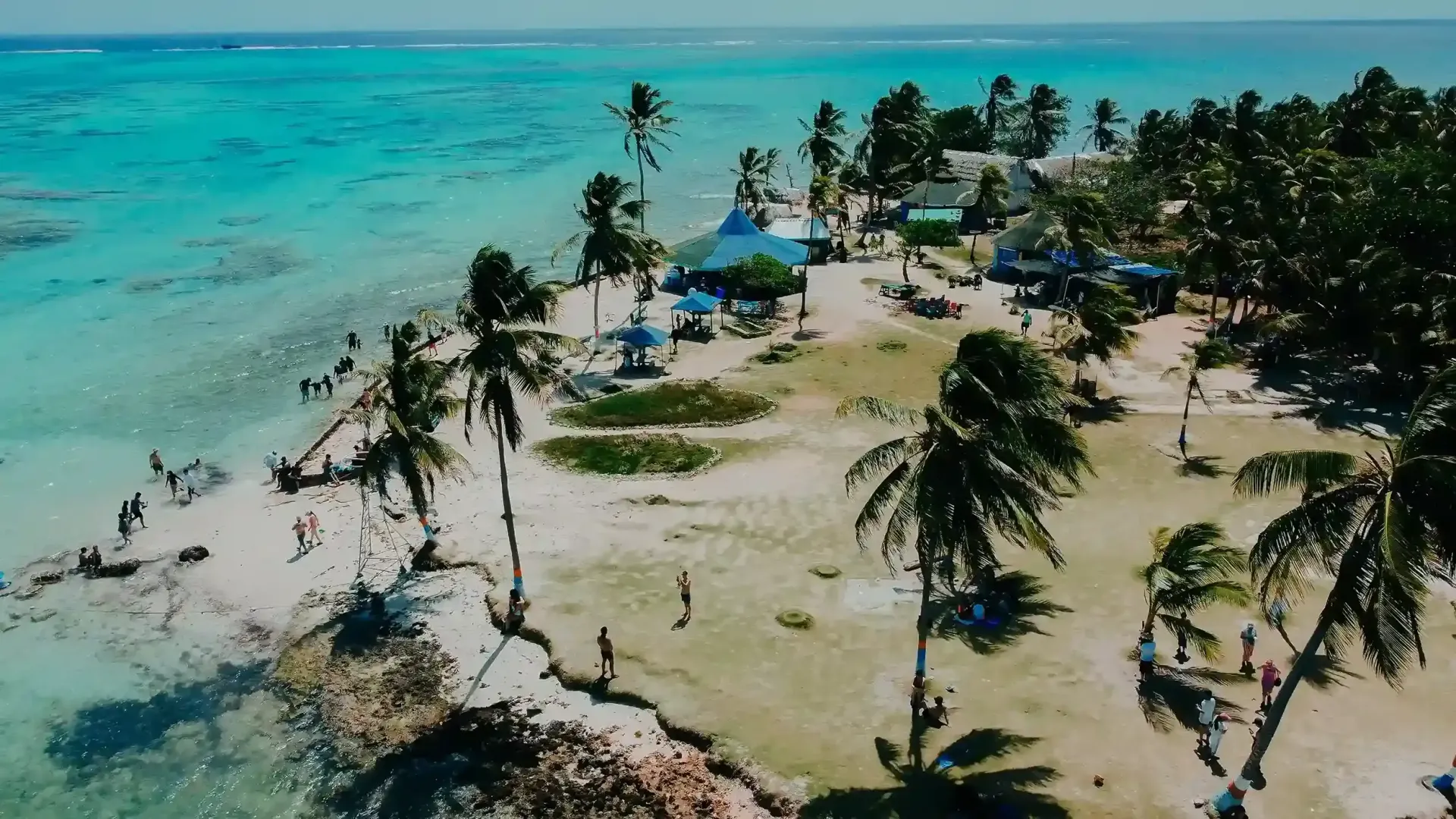 Vista aérea de las playas de San Andrés con palmeras, arena clara y mar turquesa, zona de descanso junto a la orilla.