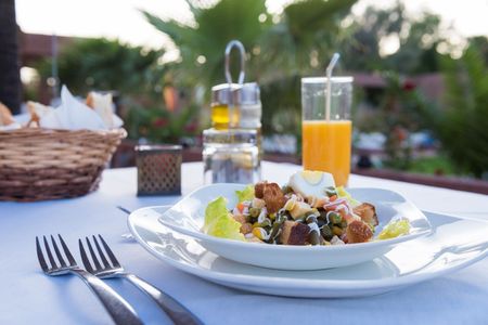 Mesa posta ao ar livre com salada, talheres, água e suco de laranja em um brunch no jardim.