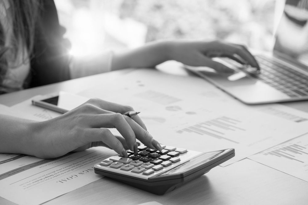 Hands using a calculator beside a laptop on a desk with paperwork - ev law in Bundall, QLD
