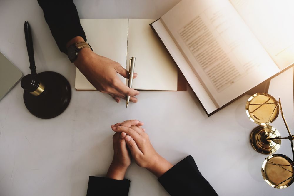 A Person Is Sitting At A Table With A Pen And A Book — EV Law In Bundall, QLD