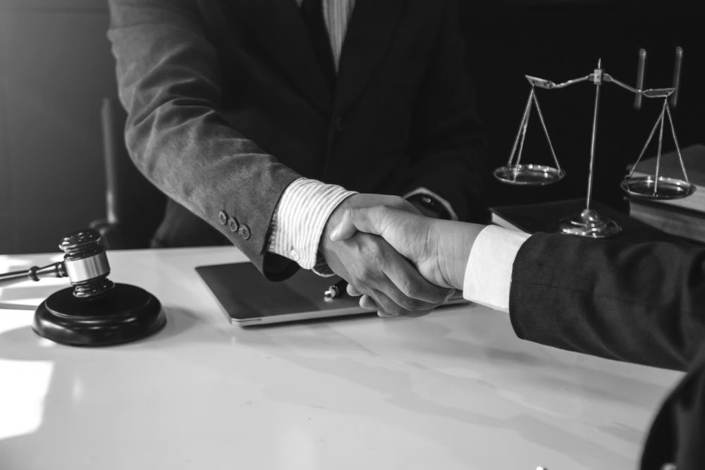 Businesspeople shaking hands at a desk with a scales of justice and a gavel in the background - ev law in Bundall, QLD