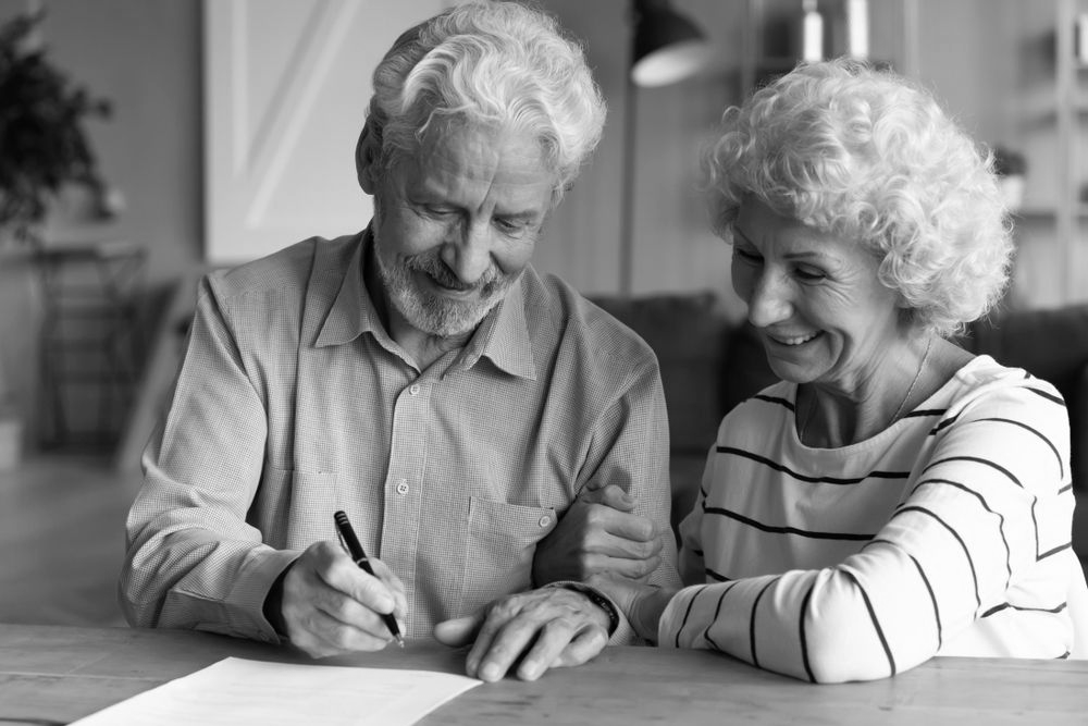 Two elderly people smiling as they sign a document at a table - ev law in Bundall, QLD