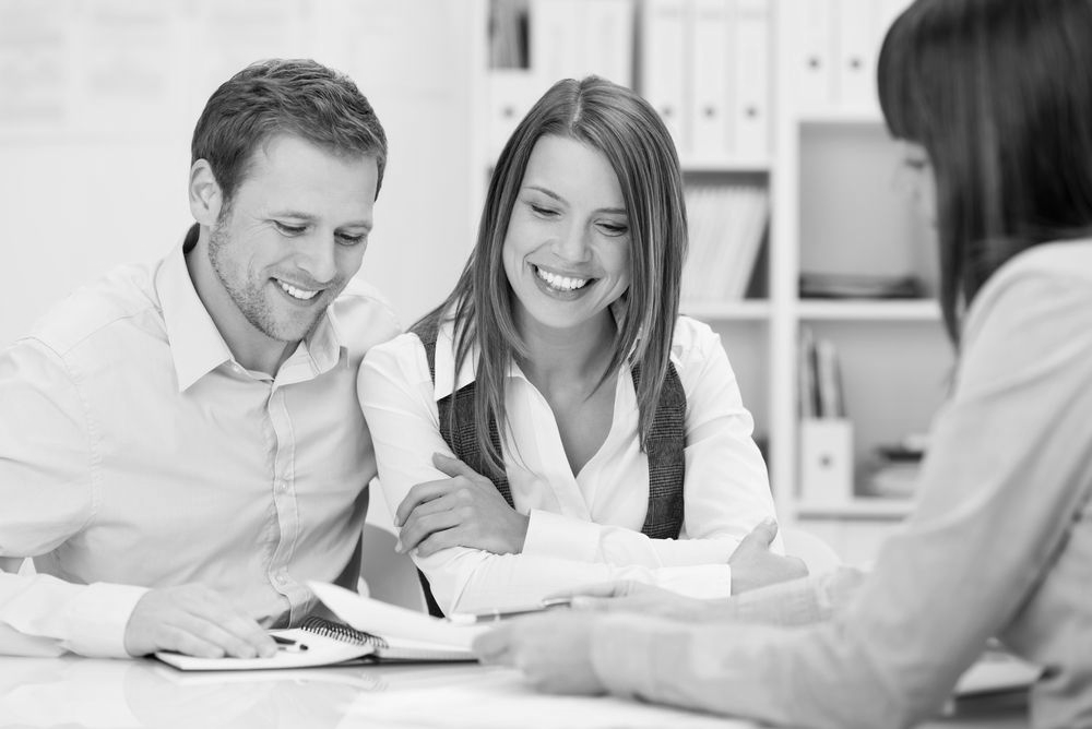 Three people in a meeting, smiling and reviewing documents at a table - ev law in Bundall, QLD.