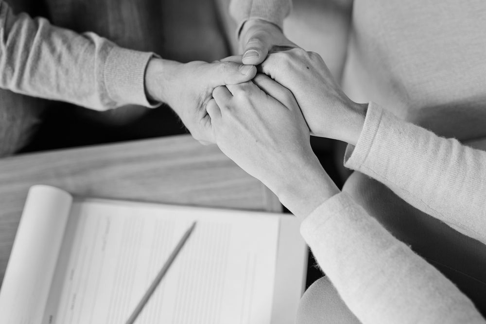 Two people clasping hands in support over a table with an open notebook and pen - ev law in Bundall, QLD