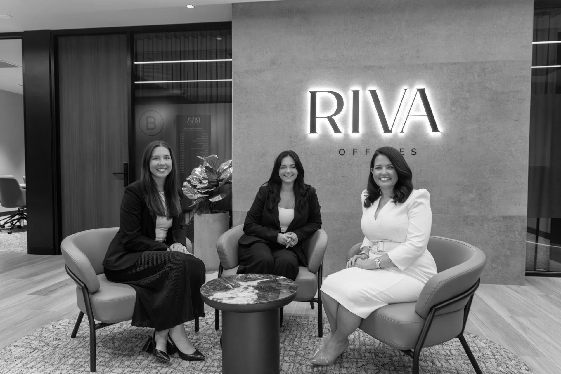 Three people seated in a lounge area beneath a glowing RIVA sign. - ev law in Bundall, QLD