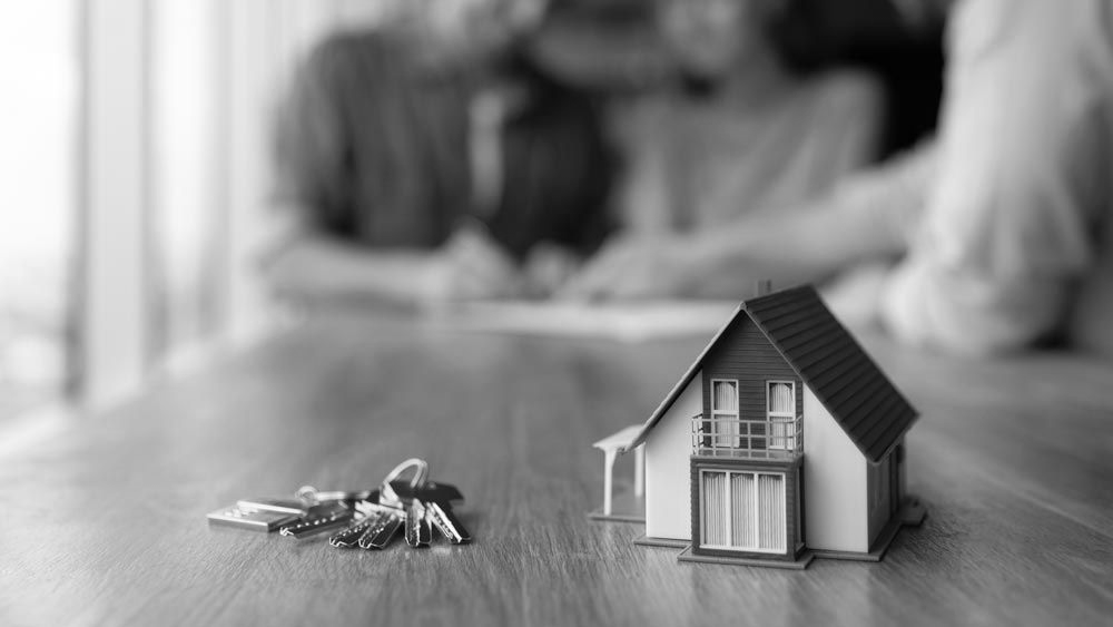 Small house model and keys on a wooden table, with a blurred couple in the background. - ev law in Bundall, QLD