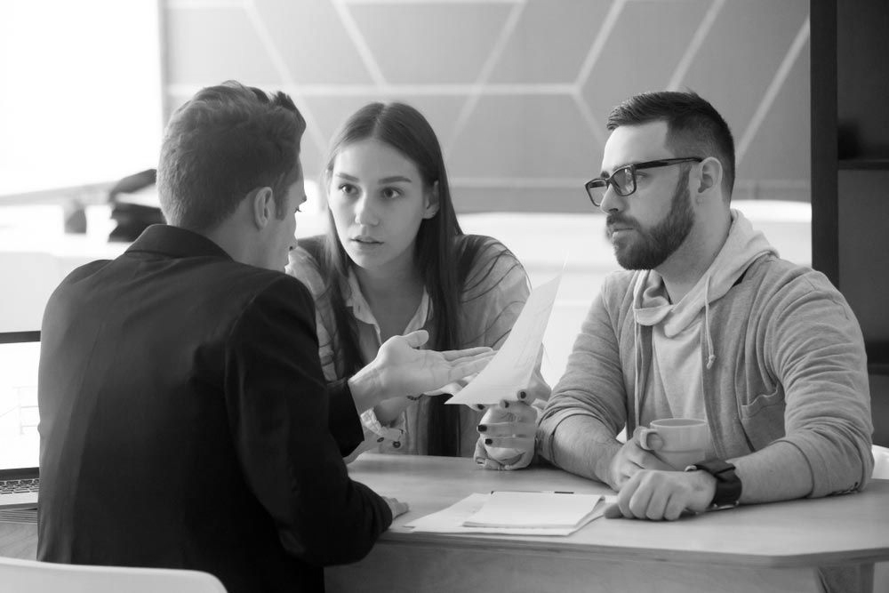Three coworkers discussing documents at a table in a modern office setting - ev law in Bundall, QLD