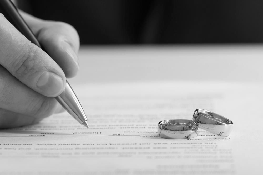 Hand signing a document beside wedding rings on a table - ev law in Bundall, QLD