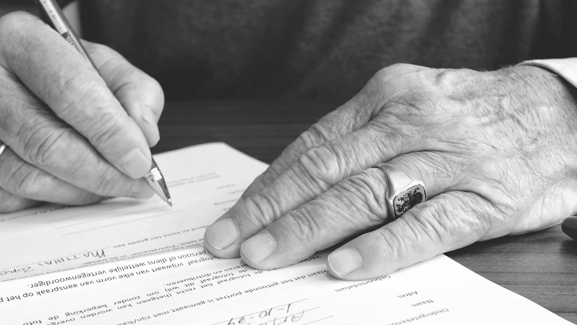Hands signing a document with a pen on a desk in black and white. - ev law in Bundall, QLD
