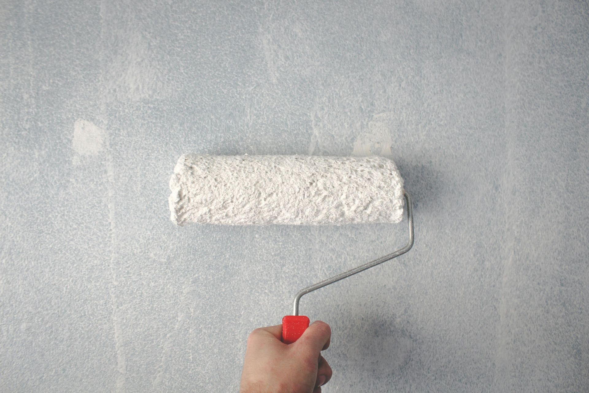 Person painting a pale blue wall with a white paint roller.