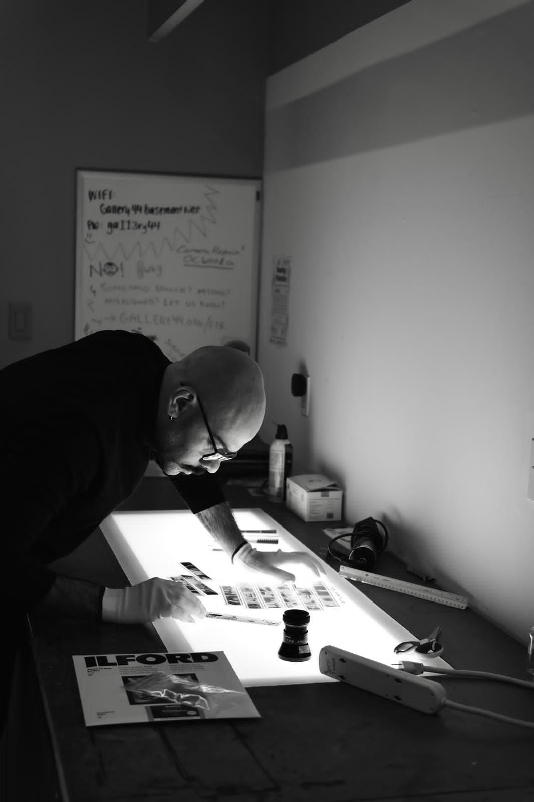 A person wearing gloves carefully examines a strip of photographic film on an illuminated lightbox in a studio.