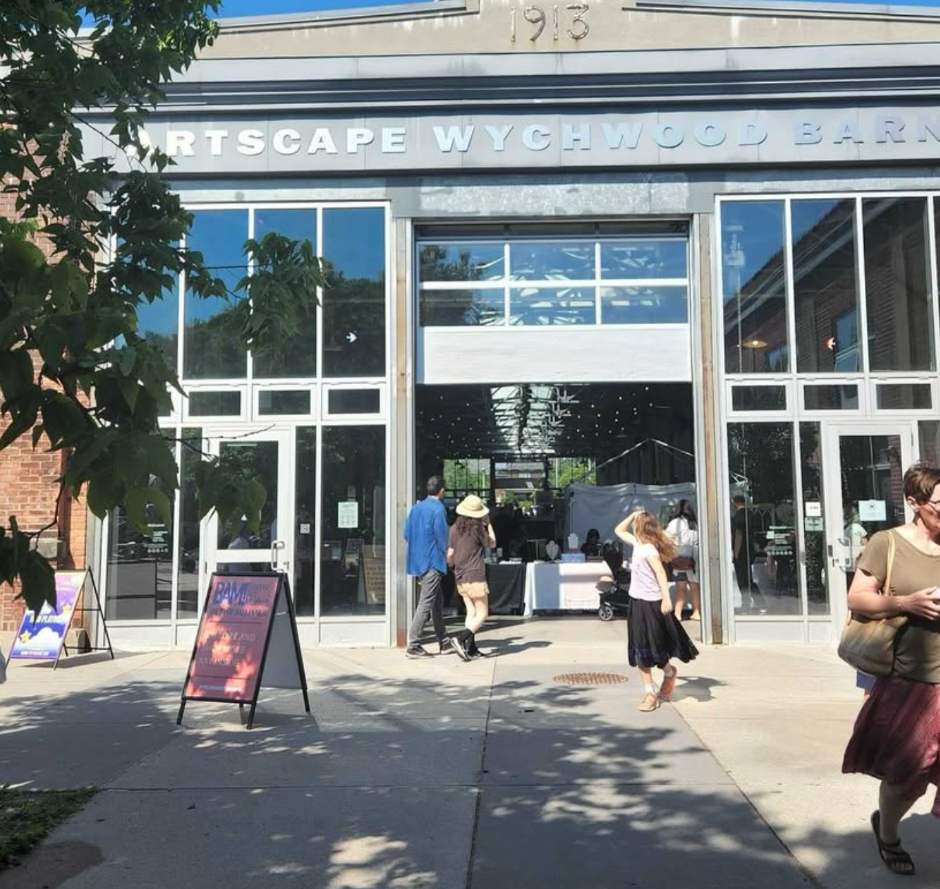 Arts building entrance with people walking in and out. Sign in foreground; brick exterior.