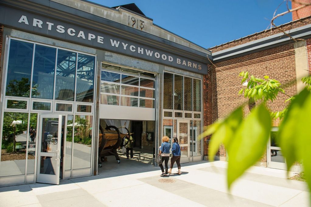 Entrance to Wychwood Barns, Toronto. Brick building with glass doors, two people walking in. Sunny day.