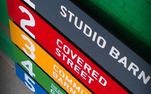 Signage with colored bars: Studio, Covered Street, Community Barn; numbers 2, 3, 4, 5, and green background.