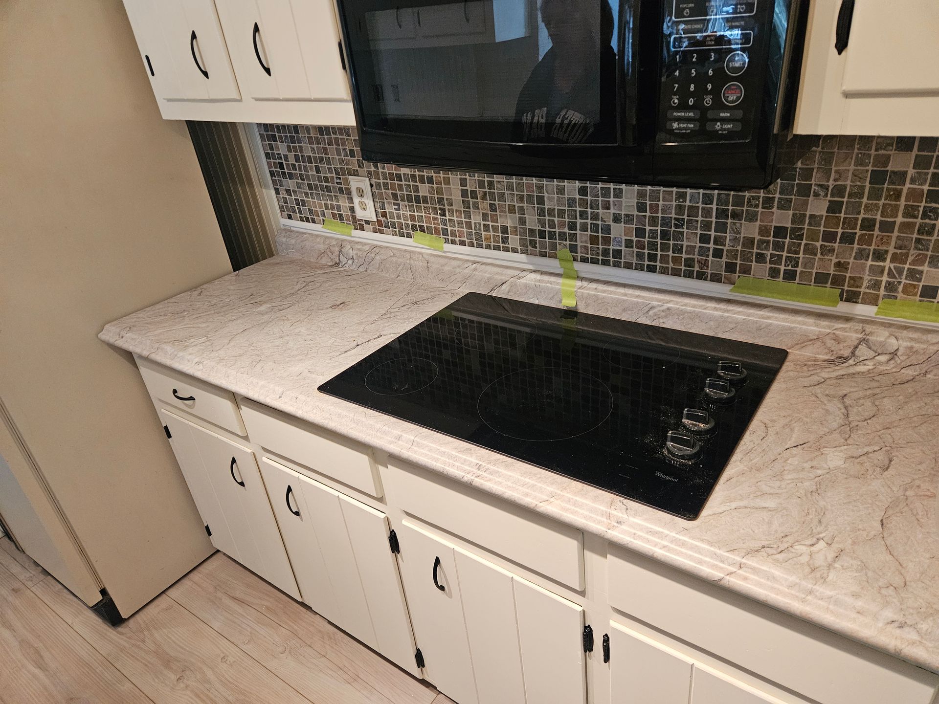 Kitchen countertop with black stovetop, white cabinets, and microwave.