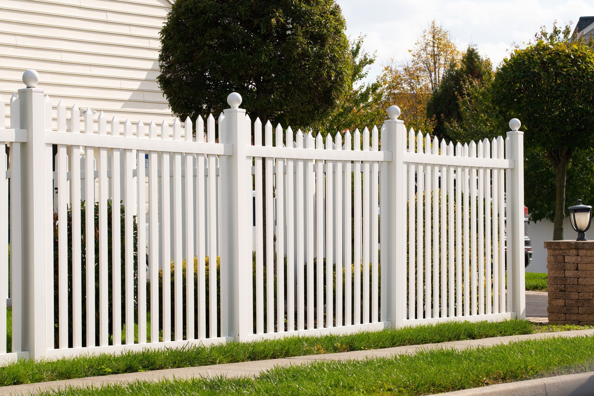 White picket fence in front of a house, along a grassy curb.