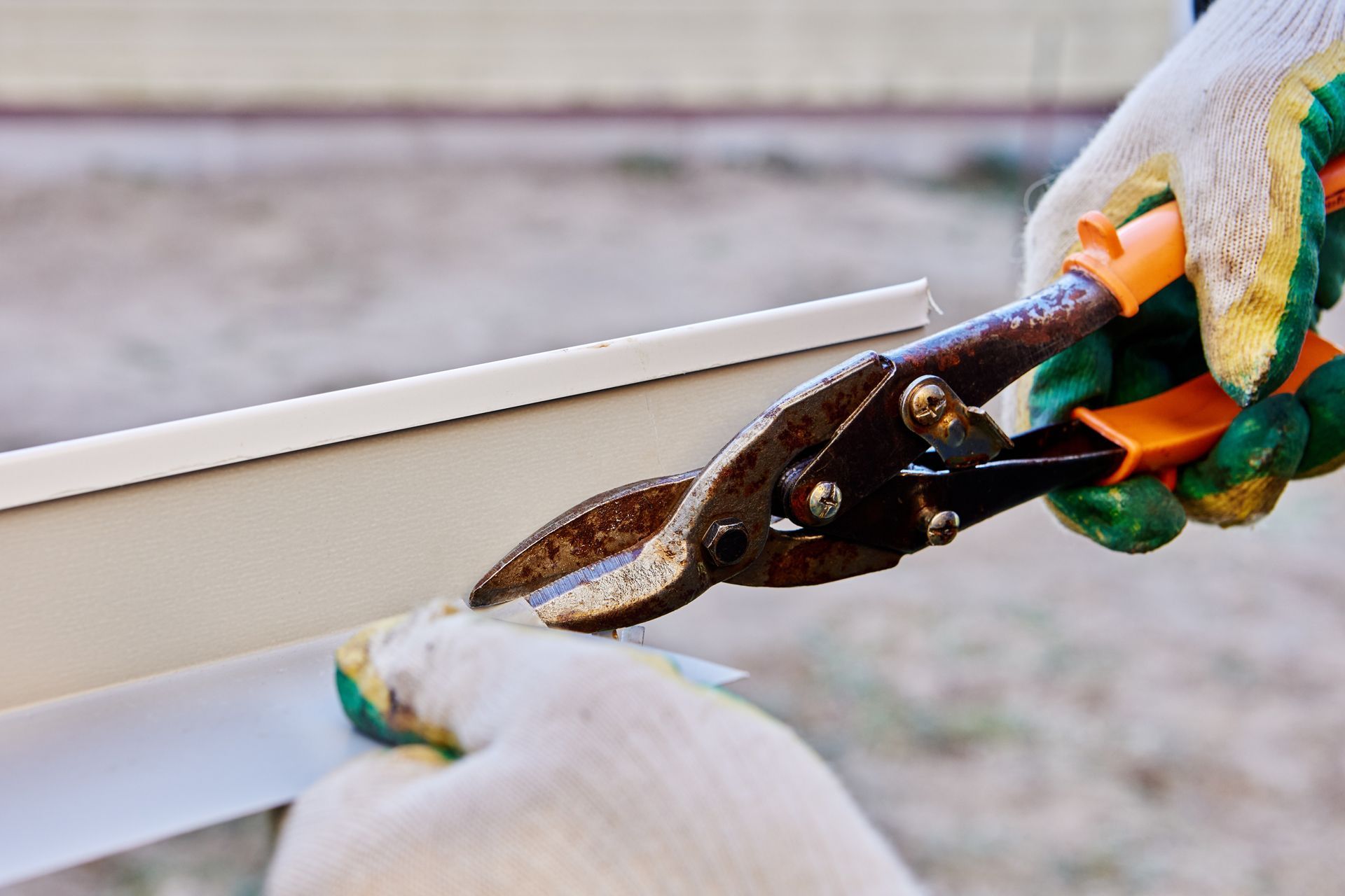 Hands in gloves cutting siding with metal shears.