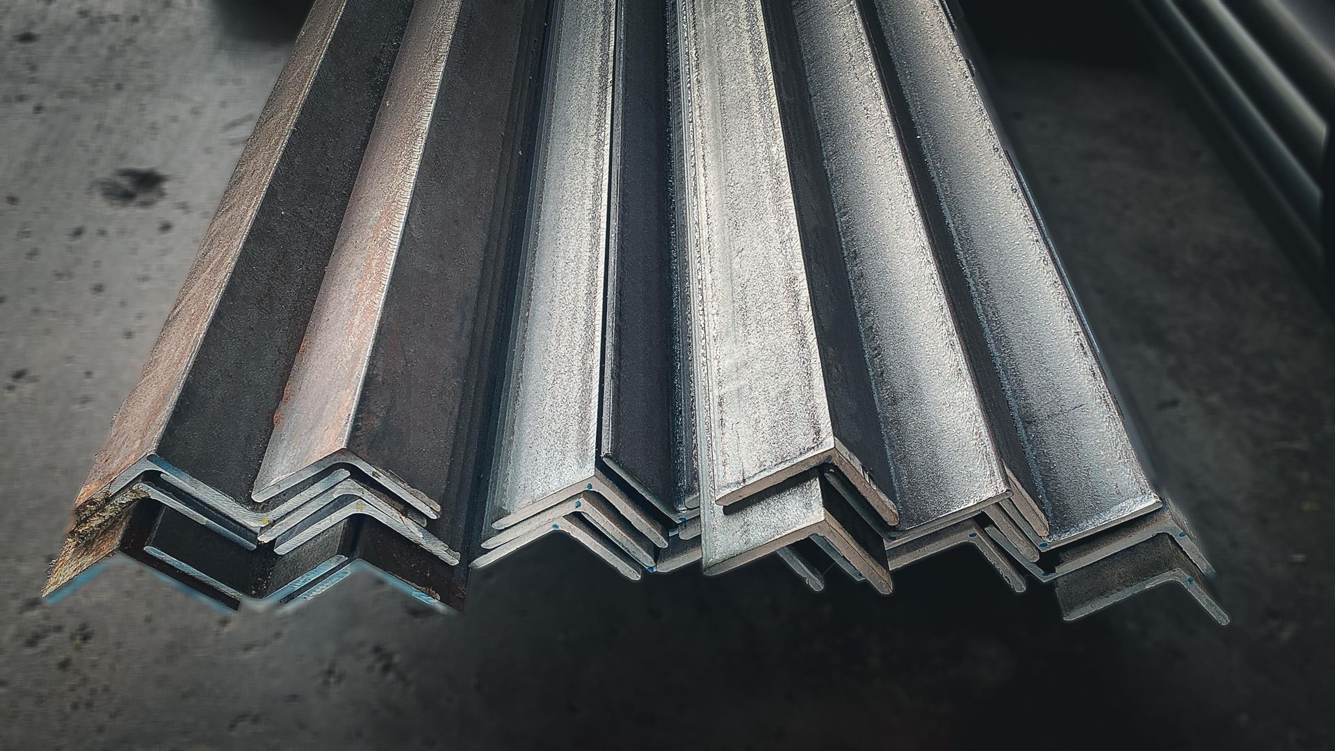 Stack of steel angle bars, gray and metallic, on a dark surface.