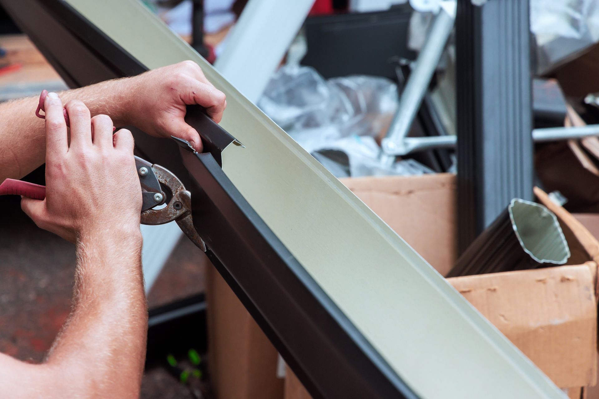 Person using metal shears to cut a section of a brown gutter.