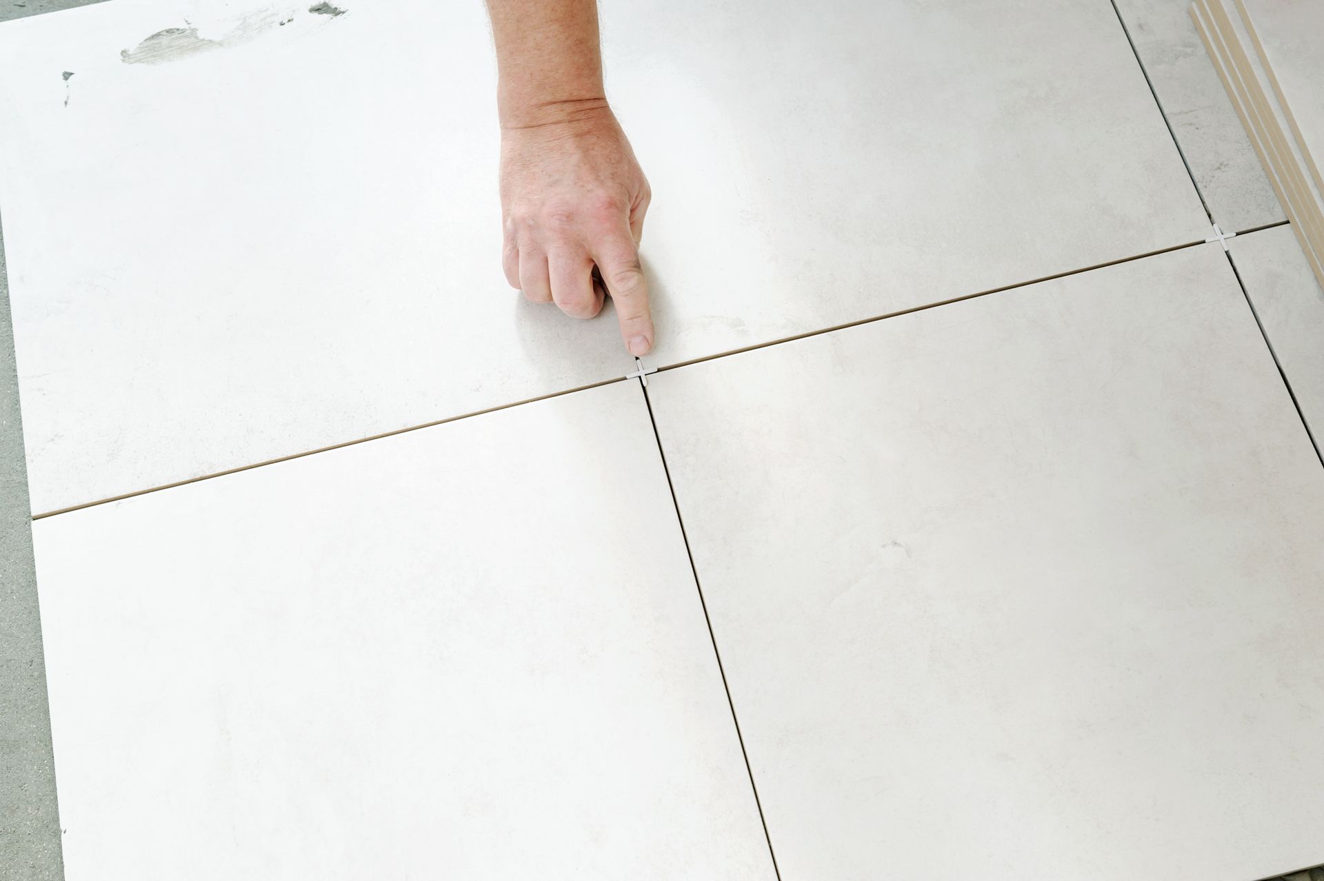 Person pointing at grout lines between large white tiles.