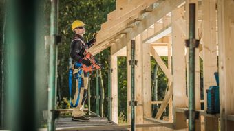 A construction worker is standing on a scaffolding holding a piece of wood