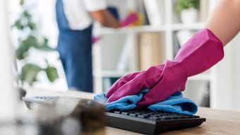 A person wearing pink gloves is cleaning a keyboard with a cloth