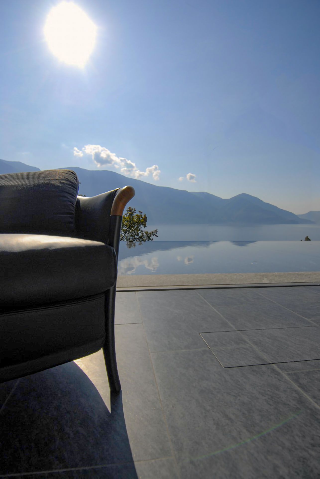 Poltrona grigia con vista sul lago sereno e sulle montagne sotto un sole splendente.
