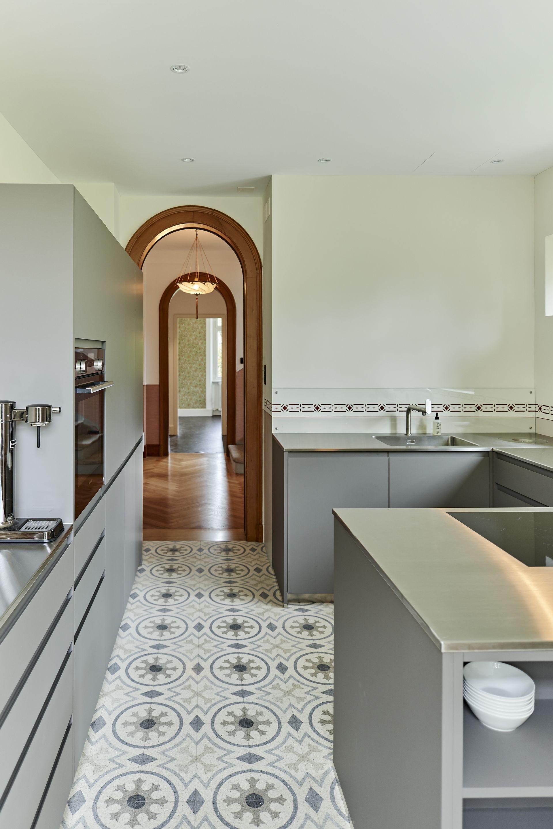 Cucina moderna con mobili grigi, pavimento decorato e porta ad arco che conduce al corridoio.
