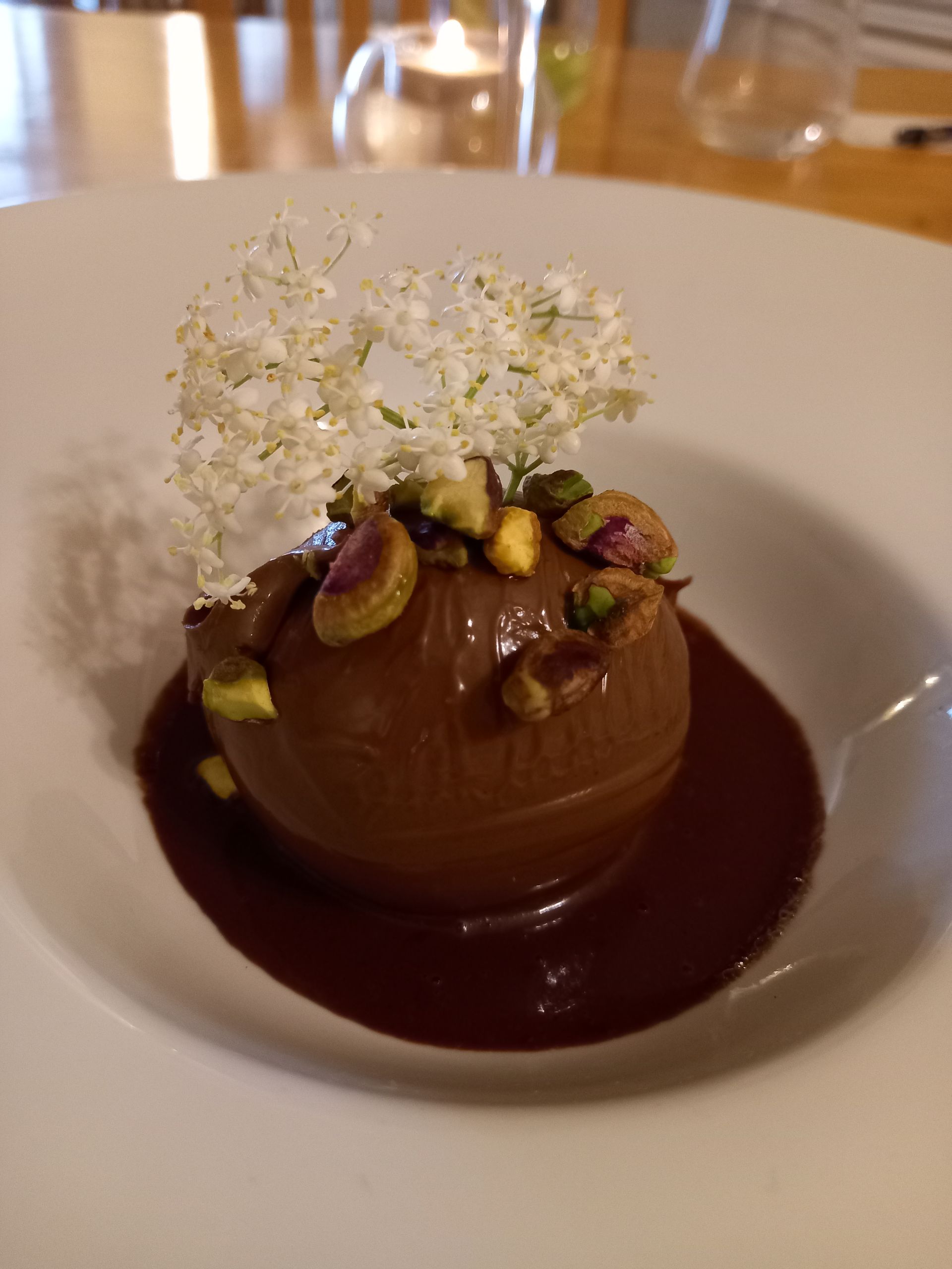 A white plate topped with a chocolate dessert with white flowers and pistachios