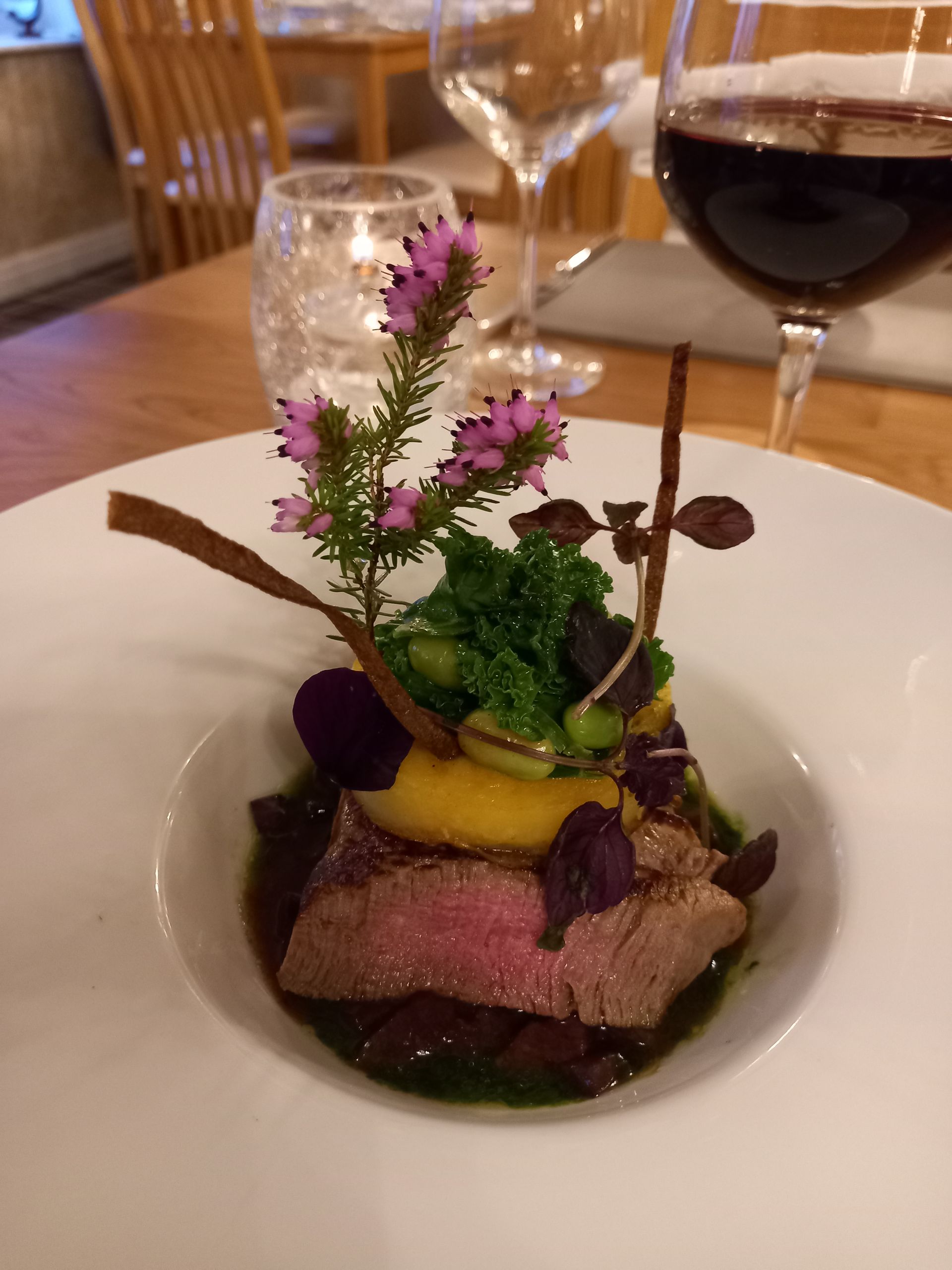 A white plate topped with meat and vegetables next to a glass of wine.