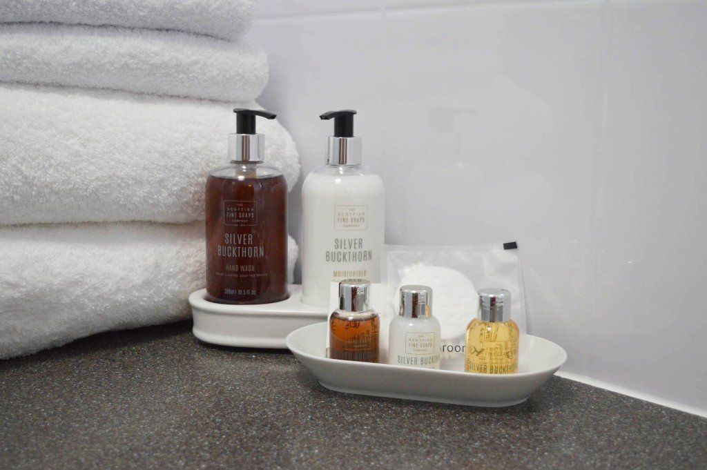 A bathroom counter with a tray of toiletries and a stack of towels.