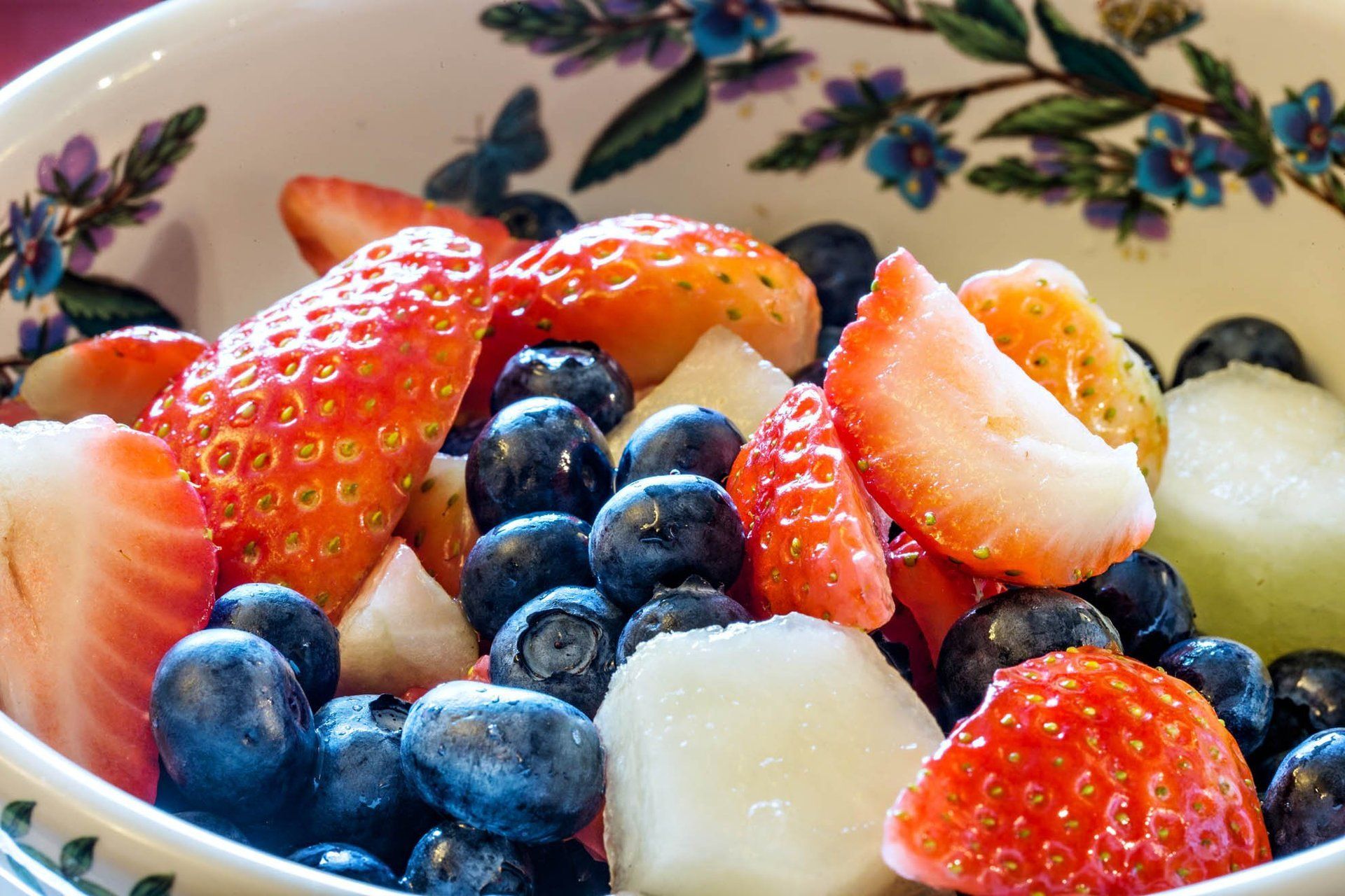 A bowl of fruit salad with strawberries blueberries and melon