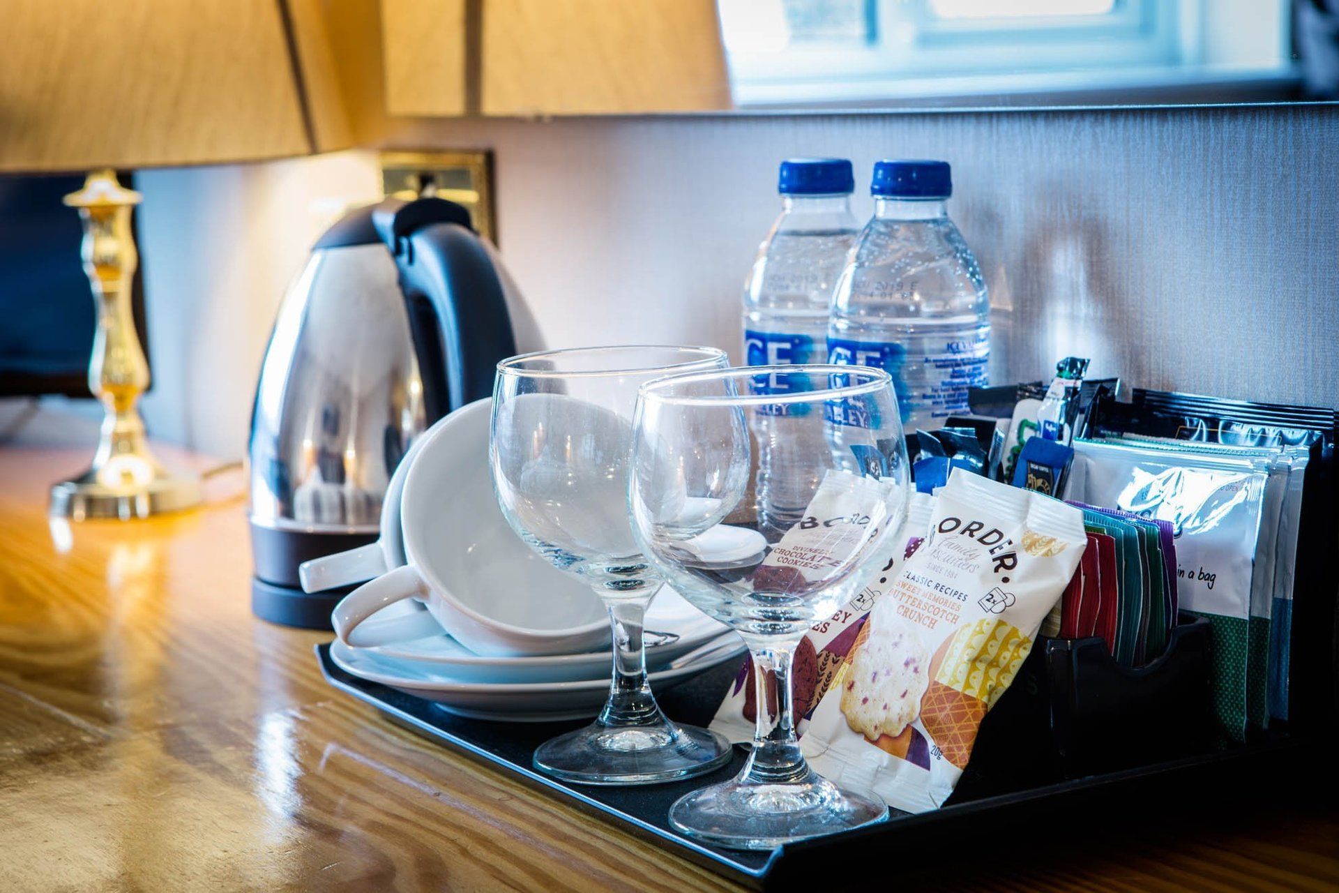 A tray with glasses , cups , and water bottles on a wooden table.