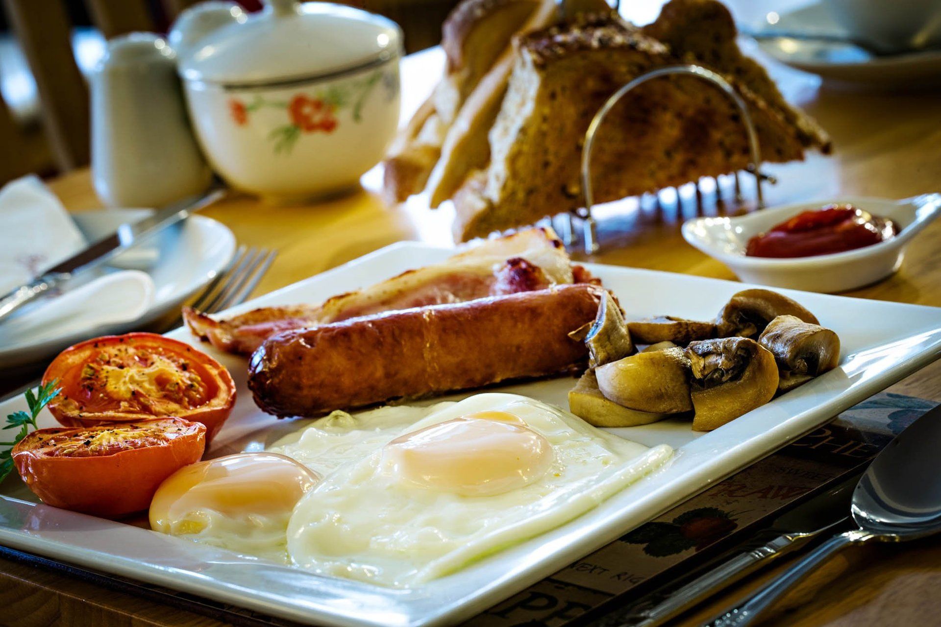 A plate of food with eggs , sausage , mushrooms and tomatoes on a table.