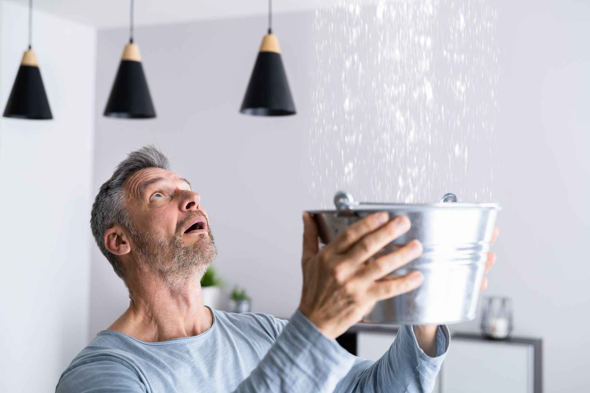 Person holding a metal bucket under a heavy ceiling leak caused by a burst pipe. Person holding a metal bucket under a heavy ceiling leak caused by a burst pipe.