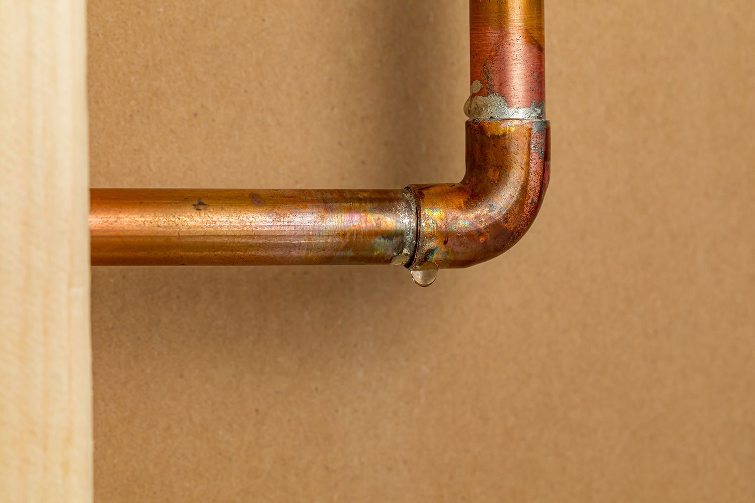 Copper pipe with a leak at a joint; water droplets visible.
