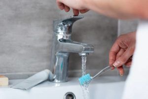 Woman Wetting Toothbrush in Sink — Lisle, IL – Jim Dhamer Plumbing and Sewer, Inc.